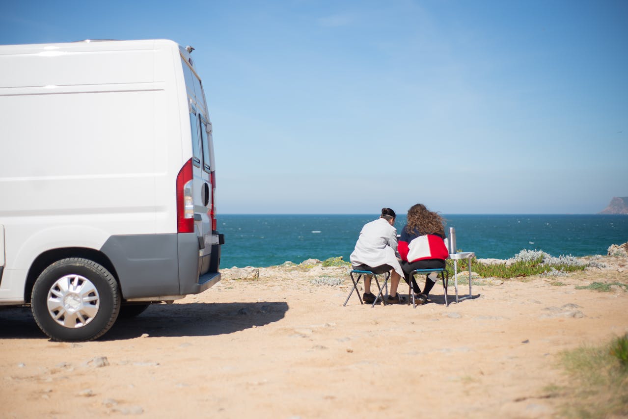 Van life couple sitting in camp chairs near the beach